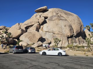 Cars parked cars near a large rock with Joshua Tree National Park in the background

Description automatically generated